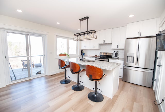 kitchen featuring white cabinetry, a center island with sink, appliances with stainless steel finishes, and decorative light fixtures