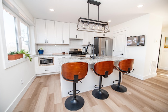 kitchen featuring hanging light fixtures, a center island with sink, white cabinetry, and stainless steel appliances