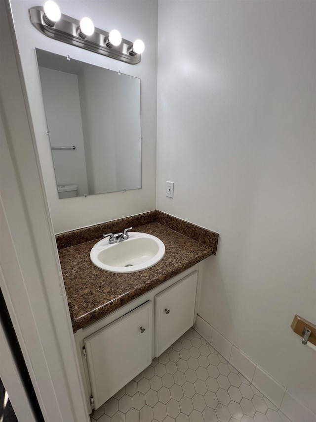 half bath with toilet, baseboards, and vanity