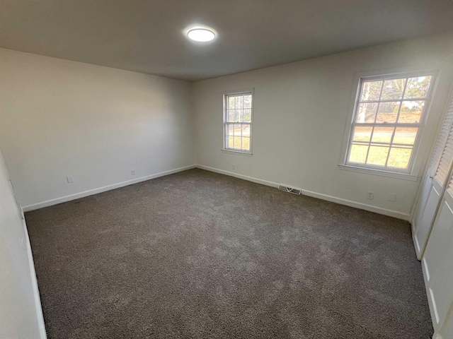 unfurnished room featuring visible vents, dark carpet, and baseboards