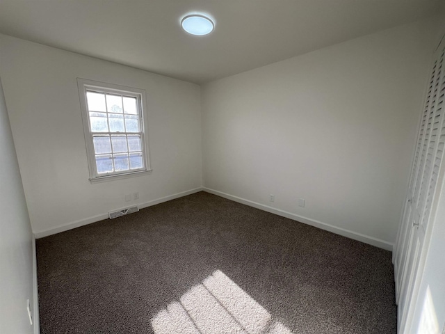 spare room featuring baseboards, visible vents, and dark colored carpet