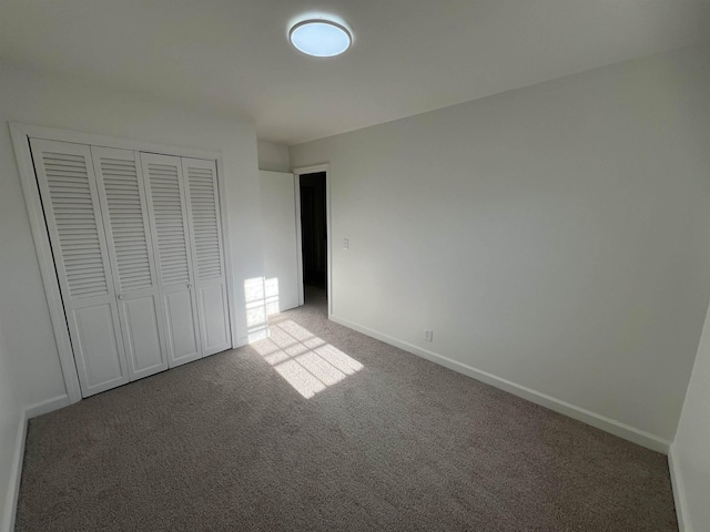 unfurnished bedroom with baseboards, dark carpet, and a closet