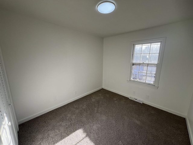 spare room with visible vents, dark carpet, and baseboards