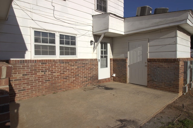 doorway to property with central AC unit, a patio area, and brick siding