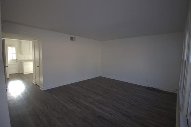 spare room with dark wood finished floors, visible vents, and baseboards