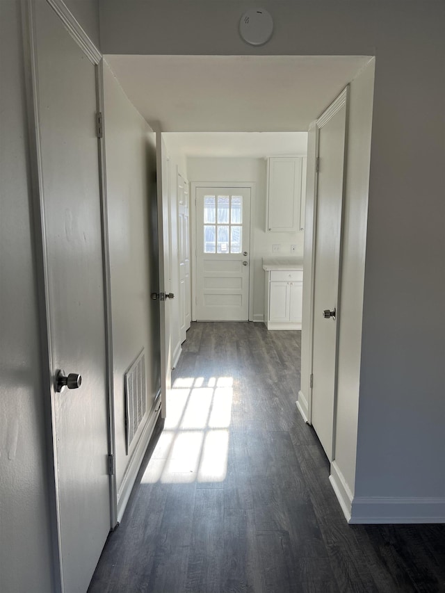 hall with baseboards, visible vents, and dark wood finished floors