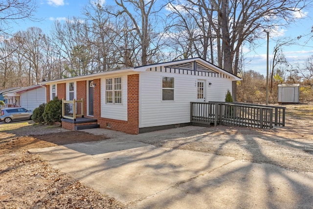 view of front of property featuring a deck, driveway, brick siding, and crawl space