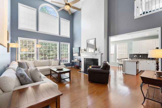 living area featuring a high ceiling, a fireplace with flush hearth, ceiling fan, wood finished floors, and baseboards