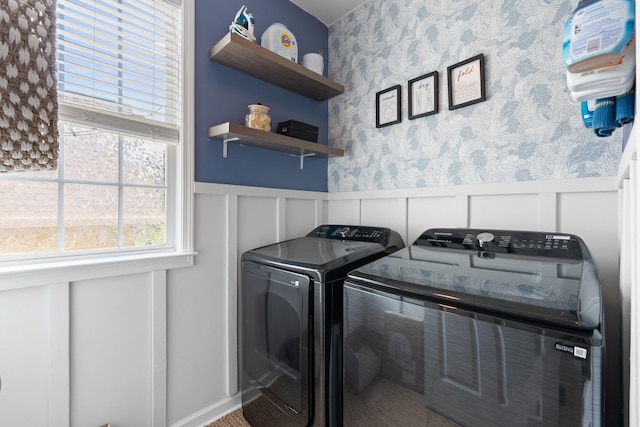 clothes washing area with wallpapered walls, laundry area, separate washer and dryer, and a wainscoted wall