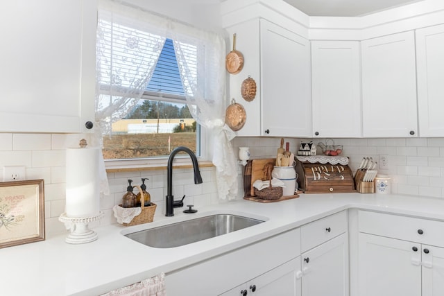 kitchen with light countertops, backsplash, a sink, and white cabinets