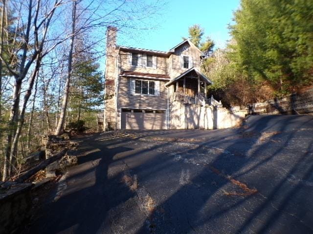 view of side of property with a garage, a chimney, and aphalt driveway