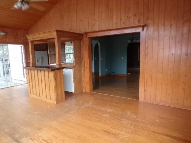 kitchen with freestanding refrigerator, vaulted ceiling, wood walls, ceiling fan, and light wood-type flooring