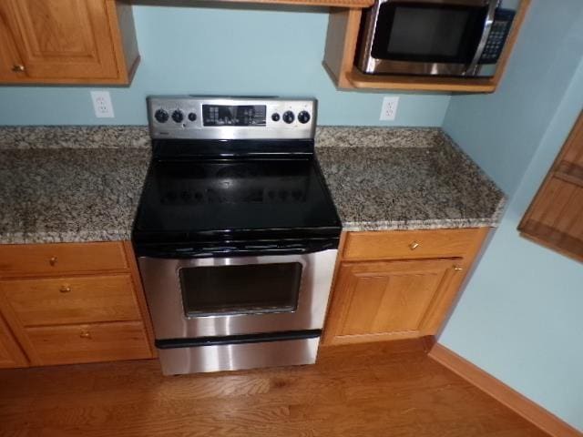 kitchen with stone counters, light wood-style flooring, and appliances with stainless steel finishes