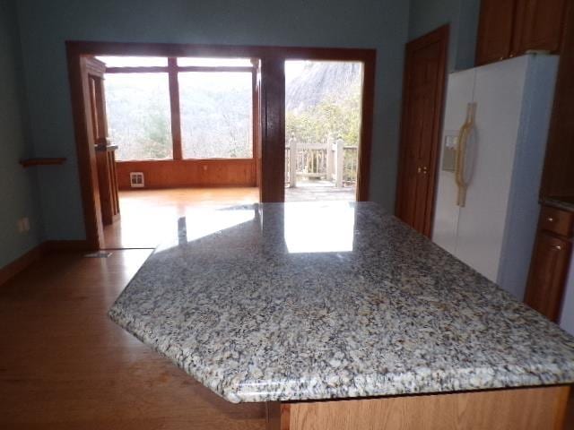 interior space featuring white fridge with ice dispenser, light stone counters, a wealth of natural light, and wood finished floors