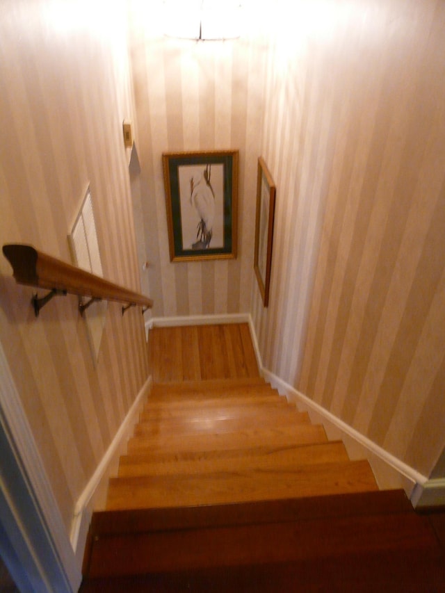 staircase featuring wood finished floors, baseboards, and wallpapered walls