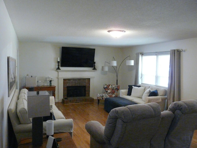 living room with a textured ceiling, a brick fireplace, and wood finished floors