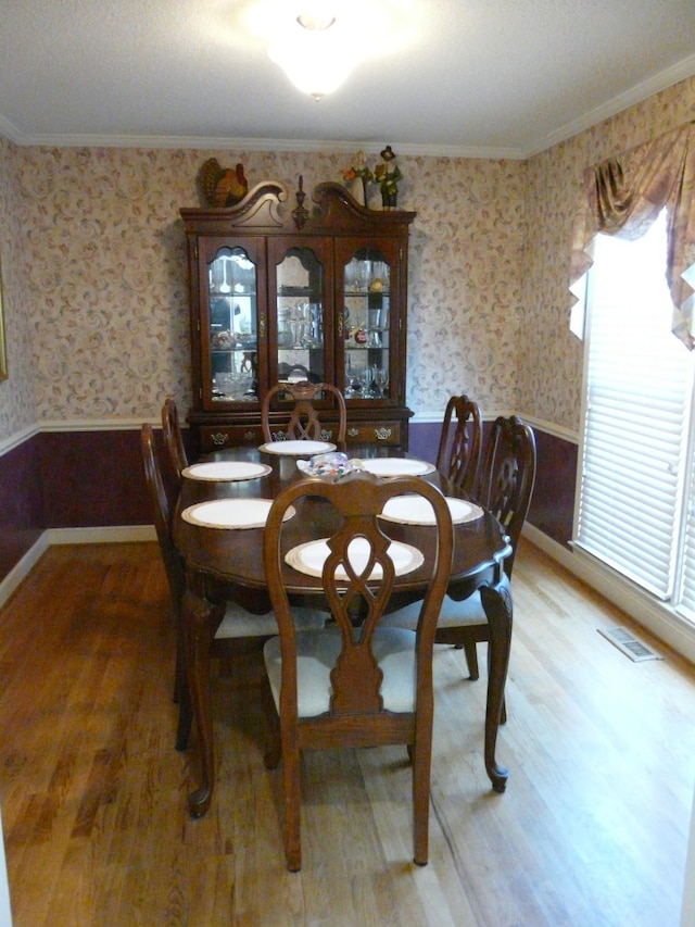 dining room with wainscoting, wood finished floors, visible vents, and wallpapered walls