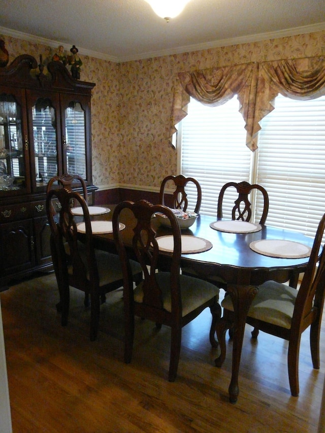 dining area with dark wood-style floors, a wainscoted wall, ornamental molding, and wallpapered walls