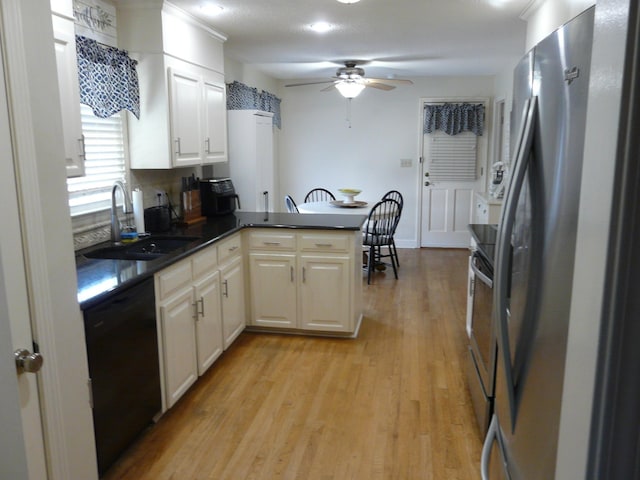 kitchen featuring a peninsula, a sink, light wood-style floors, appliances with stainless steel finishes, and dark countertops