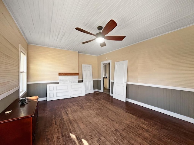 unfurnished living room with dark wood-type flooring, a wainscoted wall, and a ceiling fan