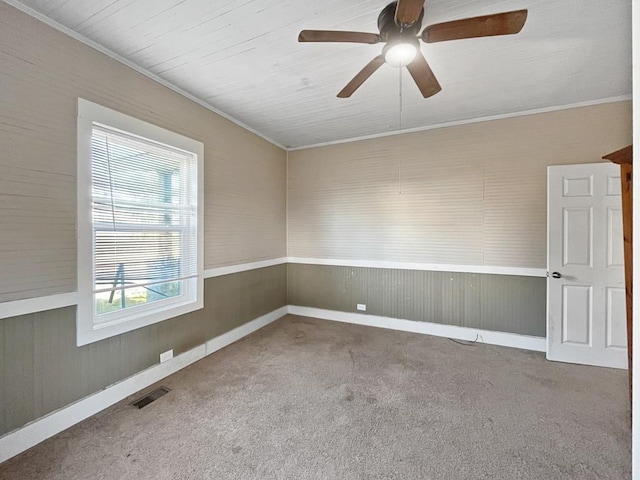 carpeted empty room with a ceiling fan, visible vents, and crown molding