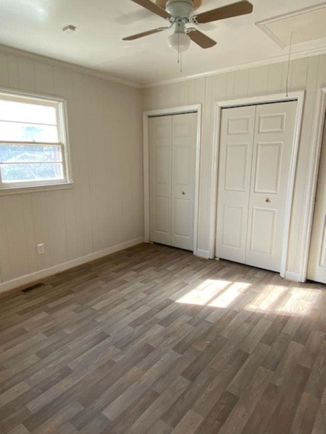 unfurnished bedroom with attic access, baseboards, ornamental molding, dark wood-type flooring, and multiple closets