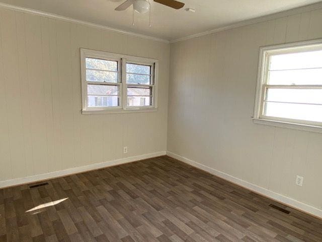 empty room featuring baseboards, plenty of natural light, dark wood finished floors, and crown molding