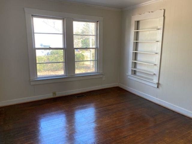 spare room featuring baseboards, visible vents, built in features, ornamental molding, and dark wood-style flooring