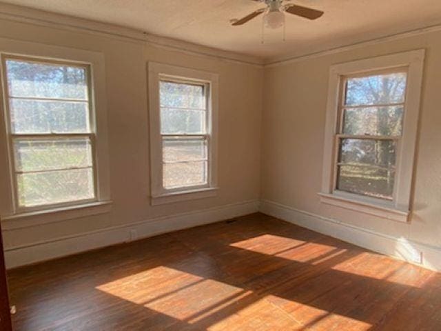 empty room with dark wood-style floors, ornamental molding, and a healthy amount of sunlight