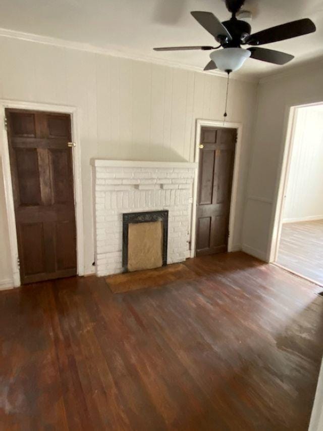 unfurnished living room featuring crown molding, dark wood-style flooring, a fireplace, and ceiling fan