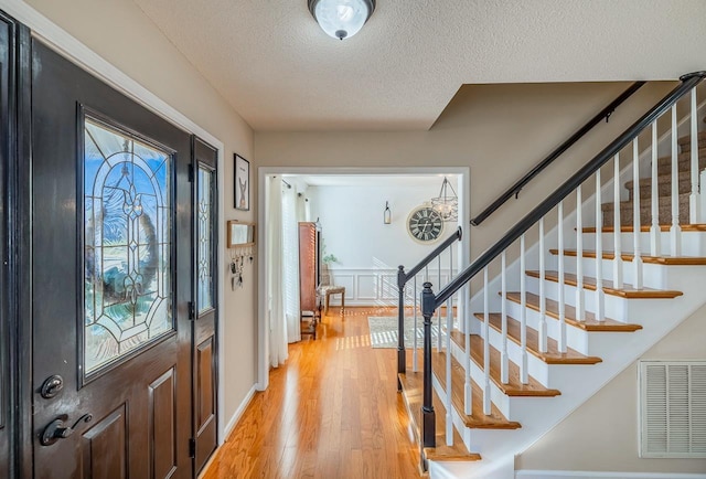 foyer entrance with a textured ceiling, light wood-style flooring, plenty of natural light, and visible vents