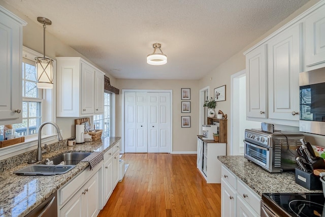 kitchen featuring white cabinets, appliances with stainless steel finishes, light wood-type flooring, pendant lighting, and a sink