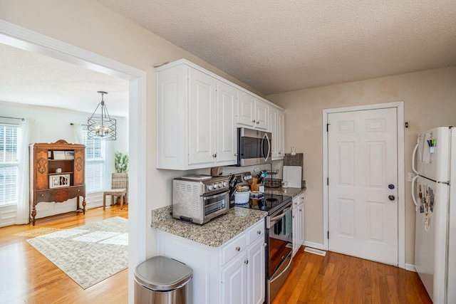 kitchen with a textured ceiling, appliances with stainless steel finishes, light wood-type flooring, and white cabinetry