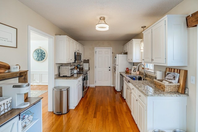 kitchen featuring light stone counters, stainless steel appliances, a sink, white cabinetry, and light wood-type flooring