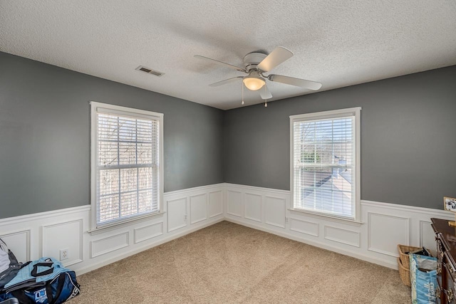 spare room with visible vents, plenty of natural light, and light carpet