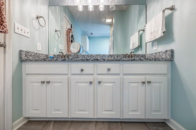 full bath with a sink, double vanity, tile patterned floors, and baseboards