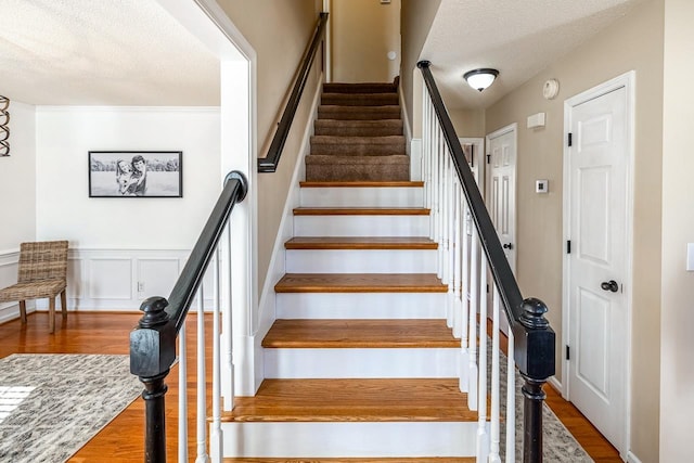 stairway with wainscoting, a decorative wall, a textured ceiling, and wood finished floors