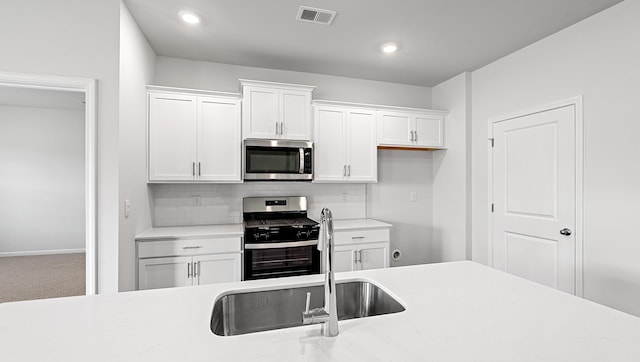 kitchen with appliances with stainless steel finishes, a sink, light countertops, white cabinets, and tasteful backsplash