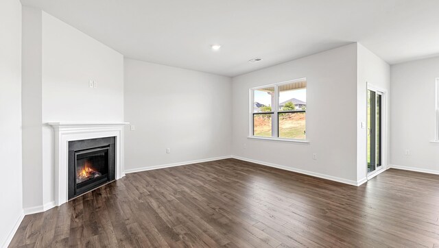unfurnished living room featuring dark wood finished floors, baseboards, and a glass covered fireplace