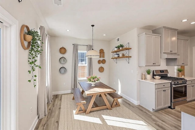 kitchen featuring light wood finished floors, gray cabinets, light countertops, gas stove, and under cabinet range hood