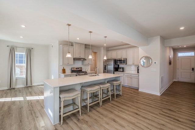 kitchen with pendant lighting, stainless steel appliances, light countertops, an island with sink, and a kitchen bar