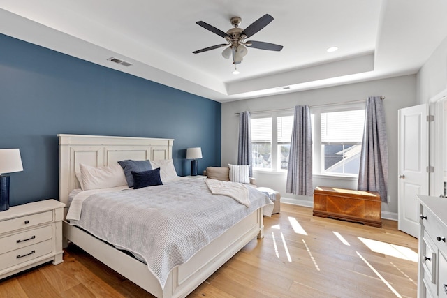 bedroom with a tray ceiling, light wood-type flooring, visible vents, and baseboards