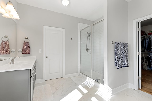 bathroom featuring marble finish floor, a shower stall, a spacious closet, and baseboards