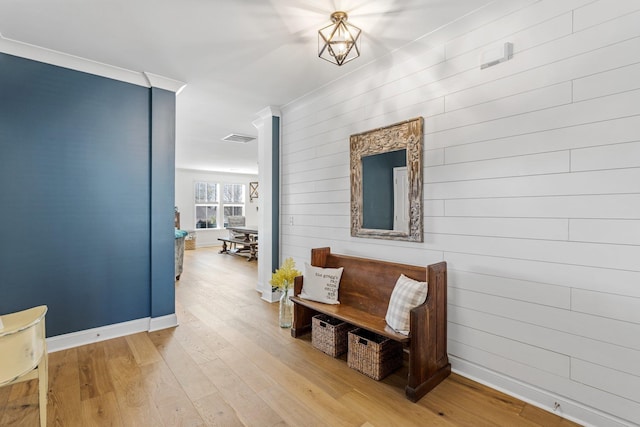 hall featuring baseboards, visible vents, wood finished floors, and ornamental molding