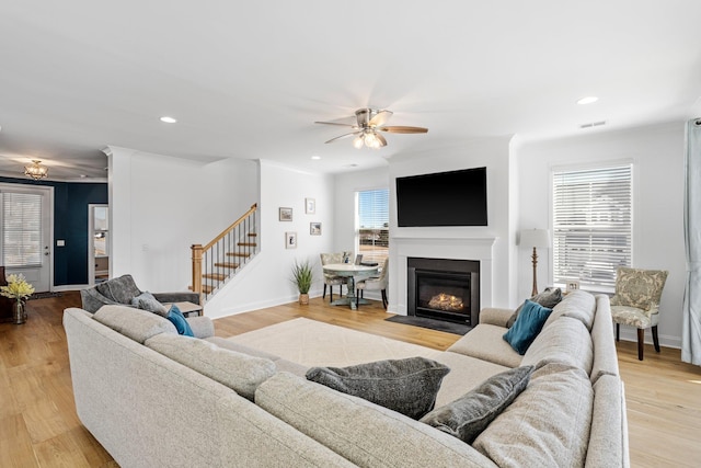 living area featuring a healthy amount of sunlight, light wood-style floors, a fireplace with flush hearth, and stairway