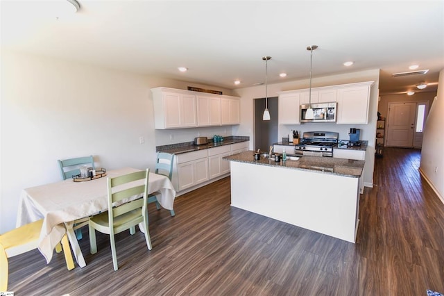 kitchen with white cabinets, an island with sink, dark wood-style floors, appliances with stainless steel finishes, and a sink