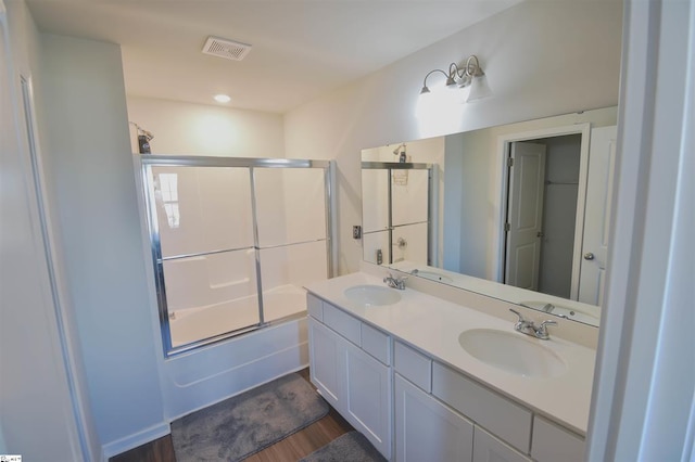 bathroom with wood finished floors, shower / bath combination with glass door, a sink, and visible vents