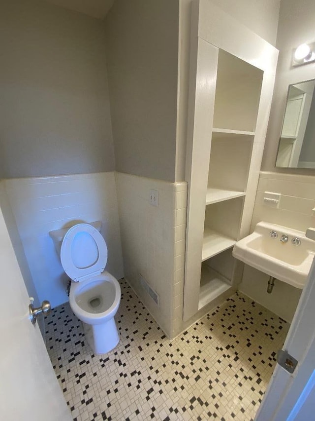 half bath with a wainscoted wall, tile walls, toilet, a sink, and tile patterned floors