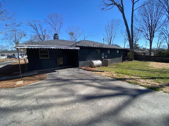 view of property exterior with aphalt driveway, brick siding, a lawn, heating fuel, and a chimney