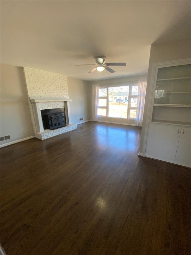 unfurnished living room with dark wood finished floors, a fireplace, visible vents, ceiling fan, and baseboards